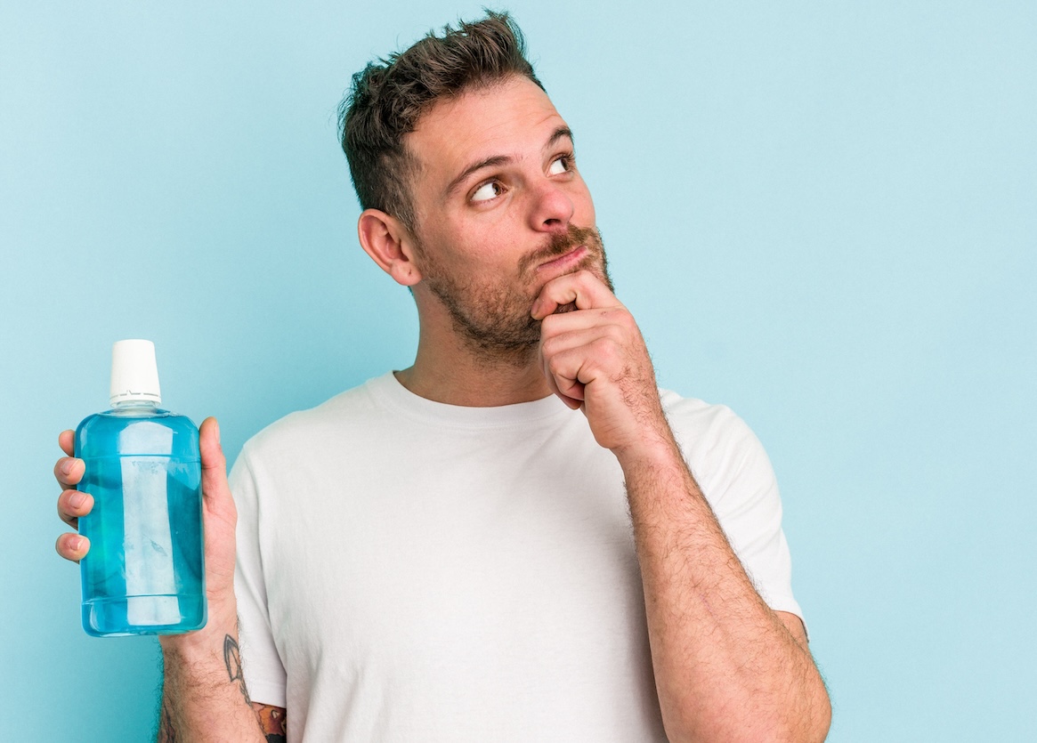 A pensive looking man holding a bottle of mouthwash