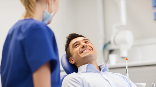 Smiling male patient in dental chair consulting with a dentist about oral health concerns