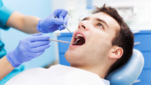 Dentist examining a male patient's gums and teeth during a dental checkup appointment